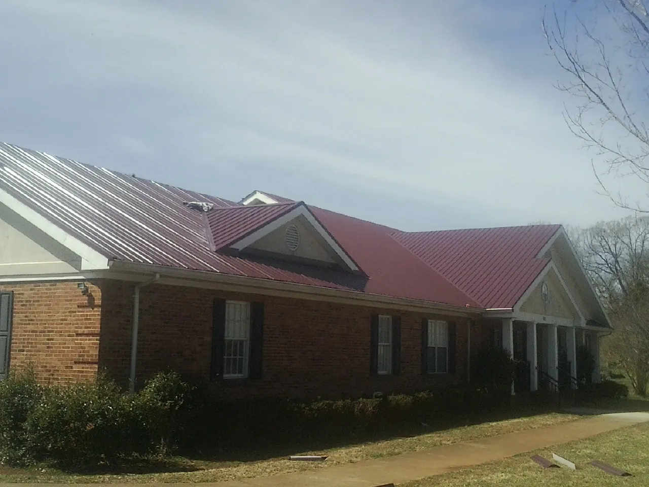 Red metal roof with gabled entries on a long brick building, from a Hail Damage Roof Repair job in Alleyton