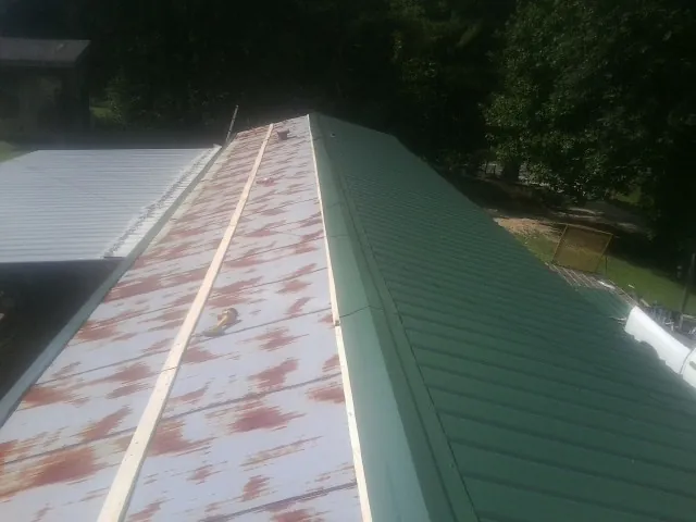 Old rusted panels beside newly installed green metal roofing — Wind Damage Roof Repair by Roofing Brothers in Alleyton