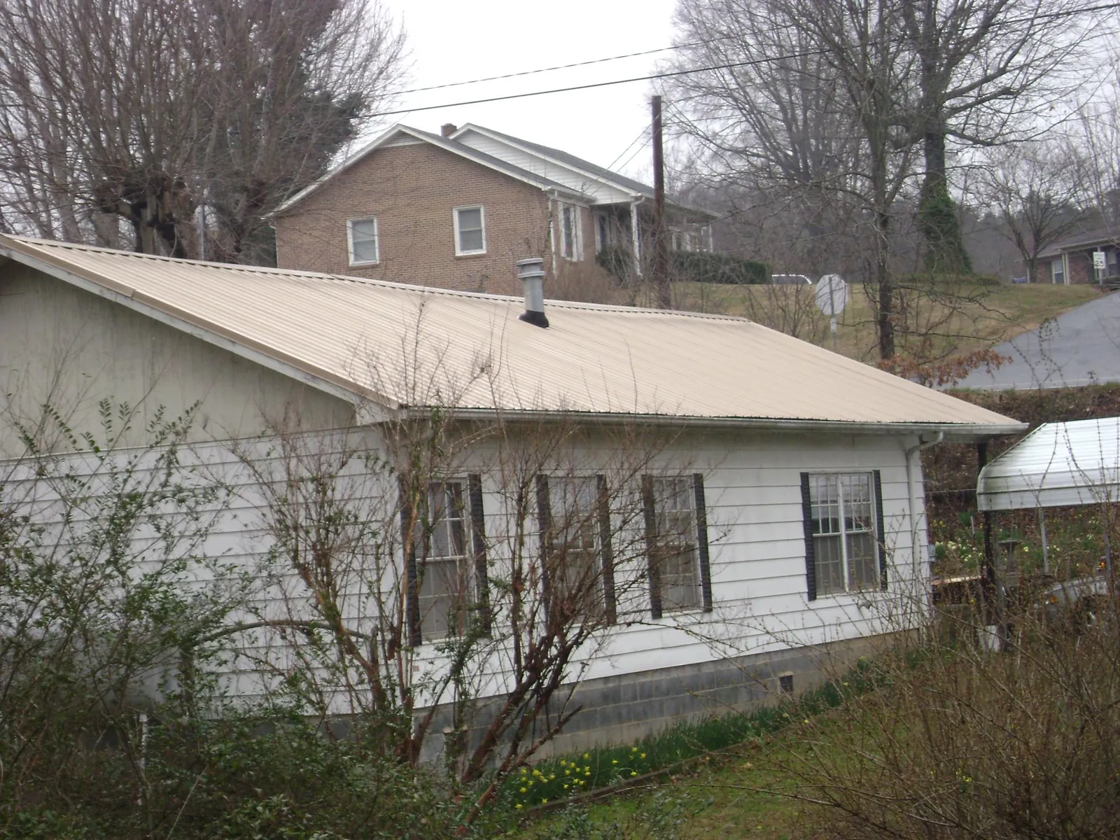 Tan metal roof on a white sided house set into a hillside — Commercial Roofing by Roofing Brothers in Alleyton