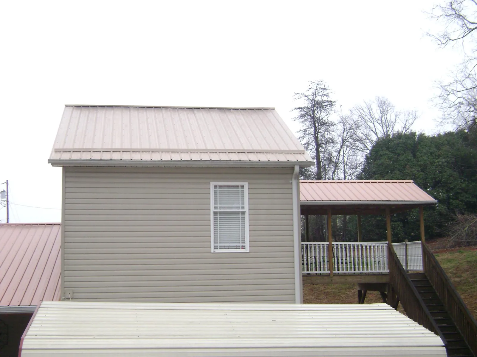 Tan metal roofs on a two story addition and attached porch, from a Roof Replacement job in Alleyton